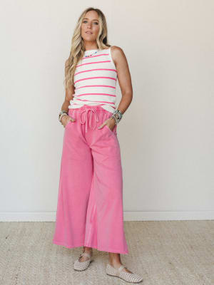 A bright, feel-good outfit pairing a cream and hot pink striped sleeveless sweater top with wide-leg cropped pink drawstring pants — styled with woven flats and layered bead bracelets for an easy, expressive look that reads playful without trying too