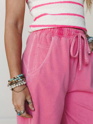 A close-up detail shot of a rosy pink washed sweatpant paired with a textured stripe crop top, styled with a stack of beaded bracelets and silver rings — casual and expressive, like a lazy Sunday that somehow looks really good.