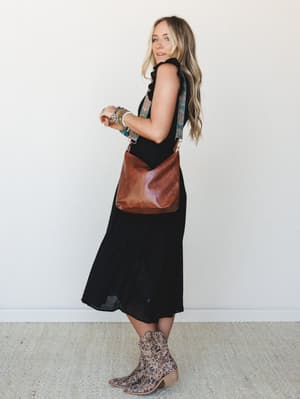 A breezy black midi dress styled with leopard print ankle boots, a cognac leather crossbody bag with a patterned guitar strap, and a stack of colorful beaded bracelets — effortless boho energy that works just as hard at brunch as it does at a concert