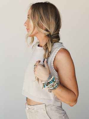 A side-profile shot of a model in a cropped sleeveless knit sweater vest and light khaki pants, her bracelet stack and stacked rings doing the most in the softest, most effortless way.