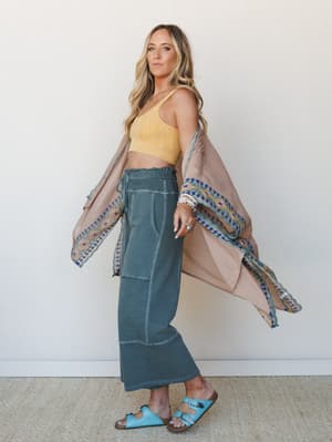 A breezy three-piece set styled together — embroidered kimono duster, lace bralette, and wide-leg pants — worn with turquoise sandals against a clean white wall, giving off that effortless 'I woke up like this but make it intentional' energy.