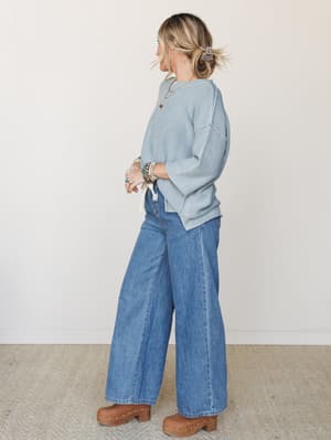 A relaxed, effortless outfit pairing a dusty blue knit sweater with wide-leg medium wash jeans and studded wood clogs — the kind of put-together-without-trying look that makes a Tuesday feel intentional.