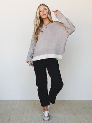 An oversized heathered knit sweater layered over a white long-sleeve tee, paired with straight-leg black pants and leopard-print sneakers — the kind of effortless, put-together look that feels cozy but intentional.