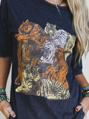 A person with long blonde hair and beaded bracelets wears the On The Prowl Distressed Graphic Tee in charcoal, featuring vintage-style tigers in orange, yellow, and white, with their hand resting near their hip.