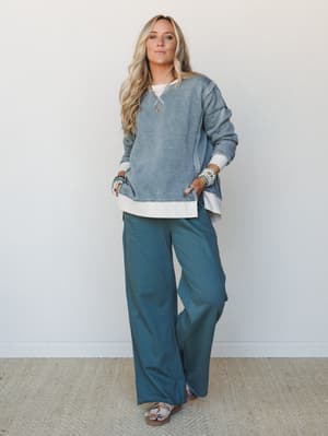 A relaxed two-piece set in tonal ash jade — an acid-wash crewneck sweatshirt layered over a white long-hem tee paired with wide-leg pants, styled with stacked beaded bracelets and sandals for that effortless, lived-in kind of put-together.
