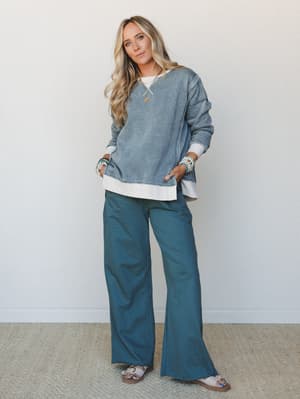 A relaxed two-piece set in muted teal tones — an oversized acid-wash sweatshirt layered over a white tee, paired with wide-leg pants — styled with beaded bracelets and sandals for an effortlessly put-together everyday look.