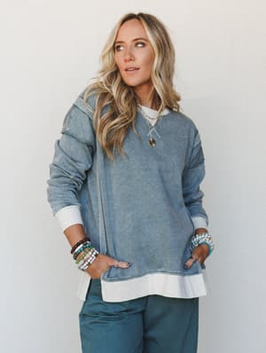 A relaxed, lived-in two-piece set in washed blue-grey styled with a layered white tee peeking out at the hem, stacked beaded bracelets, and gold layered necklaces — the kind of outfit that looks effortless but clearly wasn't an accident.