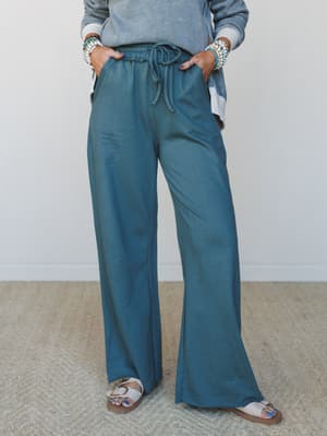 Wide-leg drawstring pants in a muted teal-jade worn with a washed sweatshirt top and Birkenstock-style sandals — the kind of effortless set that makes staying in feel intentional.