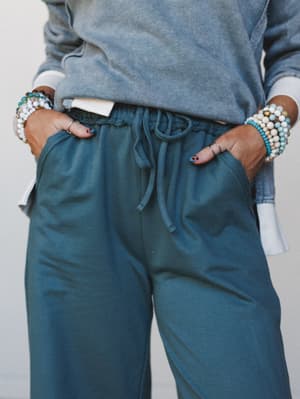 A close mid-shot of wide-leg drawstring pants in deep teal paired with a washed sweatshirt, hands tucked in pockets and stacked beaded bracelets adding just the right amount of personality.