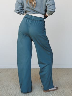 A back-view shot of wide-leg pants in a muted teal-blue paired with a cropped gray sweatshirt — the kind of cozy, intentional outfit that makes staying in feel like a whole look.