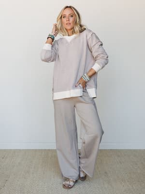A relaxed two-piece matching set in soft ash mocha — an oversized sweatshirt layered over a white tee paired with wide-leg pants — styled with beaded bracelets and footbed sandals for that effortless, I-woke-up-like-this energy.