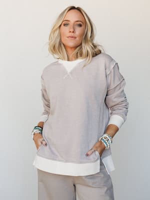 An oversized washed sweatshirt layered over a white long-sleeve tee, paired with wide-leg pants in the same muted taupe — the kind of effortless two-piece set that looks like you tried just enough, accessorized with stacked beaded bracelets for a per