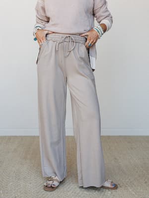 A relaxed wide-leg pant in soft ash mocha paired with a matching sweatshirt, styled with sandals and layered turquoise and pearl bracelets — the kind of effortless set that makes staying in feel intentional.