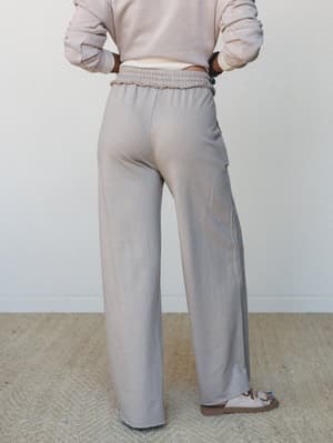 A back-view shot of wide-leg pants with a smocked waistband in a soft grey-taupe tone, paired with a cropped sweatshirt — relaxed, intentional, the kind of outfit you wear when comfort is the whole point.