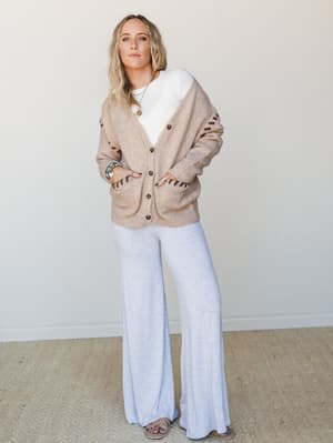 A relaxed, lived-in look built around an oversized camel cardigan with dark stitch detail layered over a white tee and breezy wide-leg heather gray pants — the kind of outfit that looks effortless but is definitely a whole mood.