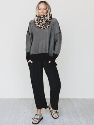 Person wearing a gray sweater, black pants, and a leopard print scarf against a white background