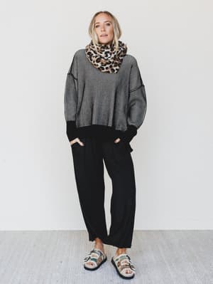 Person wearing a gray sweater, black pants, and a leopard print scarf against a white background