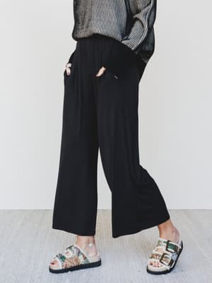 Person wearing black wide-leg pants and floral sandals on a light background