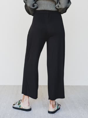 Person wearing black wide-leg pants with a striped top and floral sandals on a light background