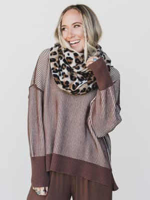 Woman wearing a brown and beige striped sweater with a leopard print scarf on a white background