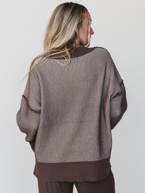 Person wearing a brown and beige striped sweater on a plain background