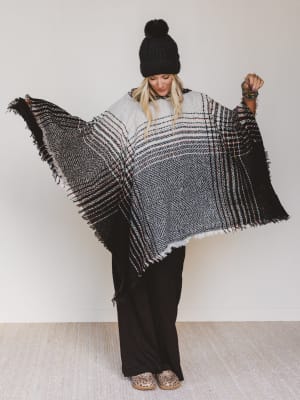 Person wearing a black and white patterned poncho against a plain background