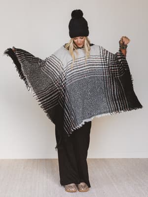 Person wearing a black and white patterned poncho against a plain background