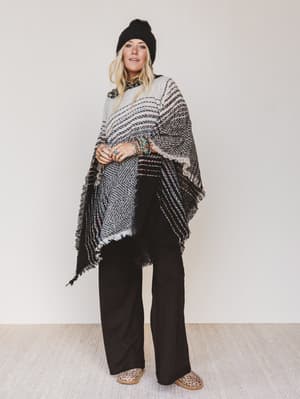 Woman wearing a patterned poncho and black pants against a white background