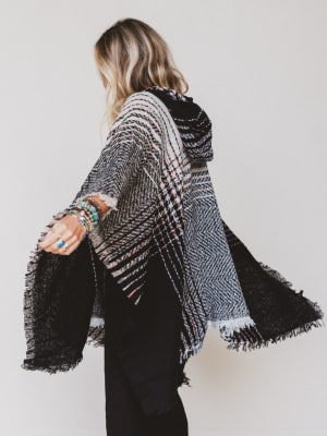 Person wearing a black and white patterned poncho against a plain background