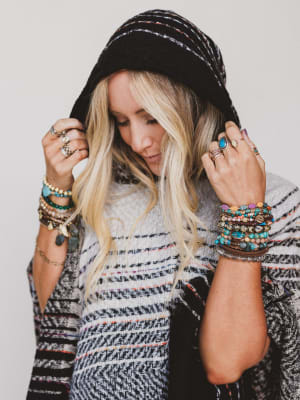 Woman wearing a black hooded jacket with colorful bracelets on a plain background