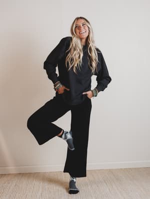 Woman in black outfit posing against a plain wall