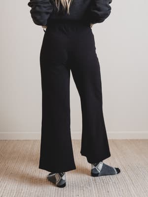Back of a person wearing black pants and a dark sweater with a plain background