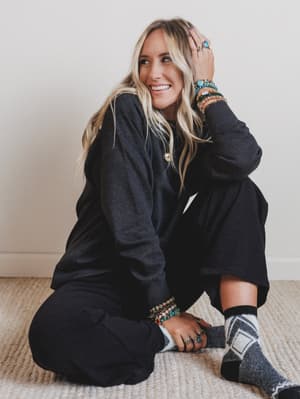 Woman sitting on a carpeted floor wearing a dark sweater and patterned socks.