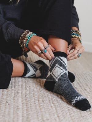 Person wearing black, gray and white patterned socks with colorful bracelets and rings on a neutral background