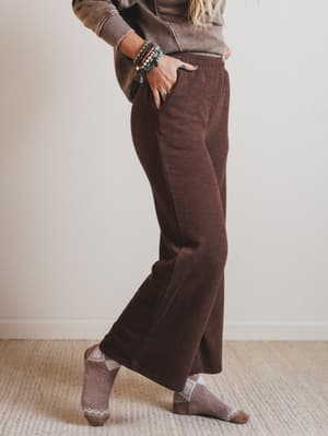 Person wearing brown corduroy pants and a sweater, standing against a plain background.