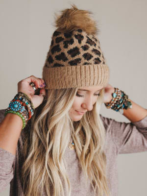Person wearing a leopard print beanie with a pom-pom, accessorized with bracelets.