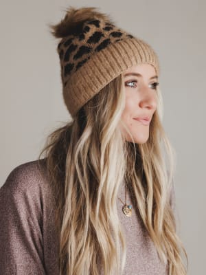 Woman wearing a brown knitted beanie with a leopard print pattern on a neutral background