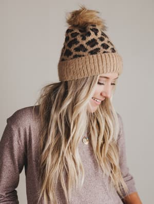 Woman wearing a leopard print pom-pom beanie against a plain background