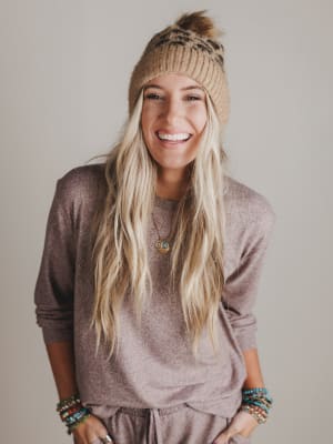 Woman wearing a brown knit beanie and sweater with a neutral background