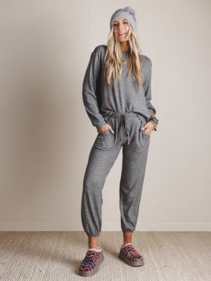 Woman wearing a gray lounge wear outfit with a beanie and patterned shoes on a plain background