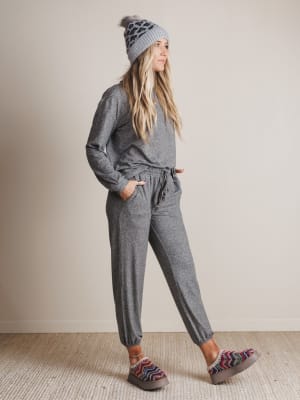 Woman wearing a gray outfit with a beanie and patterned slippers on a neutral background