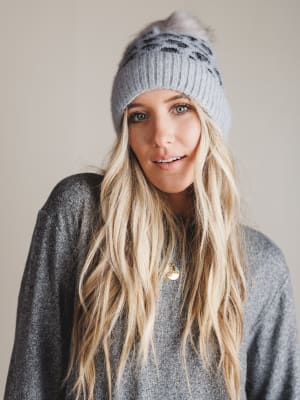 Woman wearing a gray leopard print knit beanie with pom-pom on a plain background