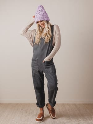 Person wearing a gray jumpsuit and purple knit hat against a plain background