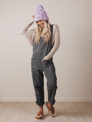 Person wearing a gray jumpsuit and purple knit hat against a plain background