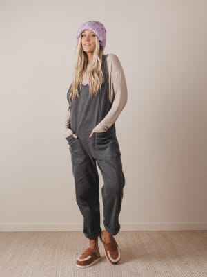 Woman wearing a gray jumpsuit, beige cardigan, and brown shoes against a plain background