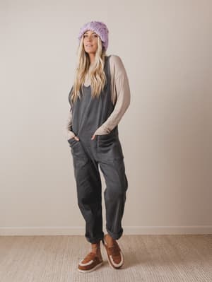 Woman wearing a gray jumpsuit, beige cardigan, and brown shoes against a plain background