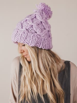 Person wearing a purple knit beanie with a pom-pom against a neutral background