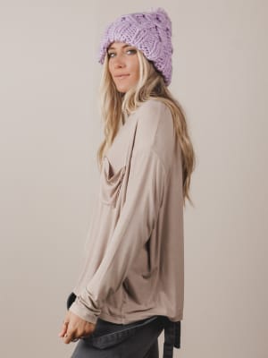 Woman wearing a beige long-sleeve top and a purple knitted hat against a plain background