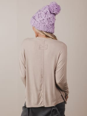 Person wearing a beige jacket and purple knit beanie against a plain background