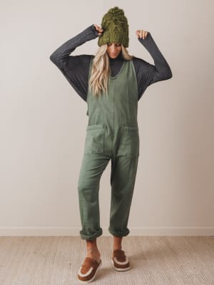 Person wearing green overalls and a knit hat against a plain background